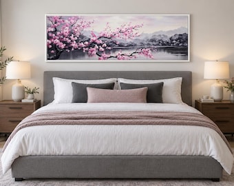 May include: A rectangular wall art print featuring a landscape painting of pink cherry blossom branches extending over a calm lake with distant mountains in the background, all enclosed within a thin white frame mounted above a gray upholstered bed.