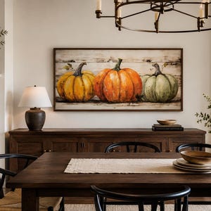 May include: A rectangular wall art piece featuring a painting of three pumpkins in yellow, orange, and muted green colors, set against a horizontal white wood plank background, all enclosed within a simple dark brown wooden frame.