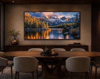 May include: A large rectangular wall art print featuring a landscape of snow-capped mountains, a dense forest of evergreen trees, and a calm lake reflecting the golden sunset light, displayed in a dining room above a dark wooden sideboard.