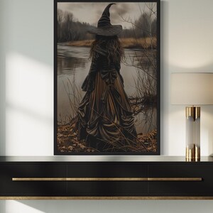 a large framed artwork depicting a woman in a long dress standing by a lake, with a witch's hat on her head. The artwork is hanging on a wall, and there is a black console table below it.