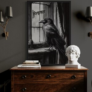 May include: A framed black and white artwork featuring a raven perched on a windowsill, with the word "Nevermore" above. The artwork is displayed above a wooden dresser, with a bust and books. Two wall sconces with black shades flank the artwork.