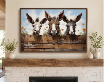 May include: A rectangular wall art print in a dark wood frame depicting three donkeys with white, brown, and grey fur peering over a weathered, horizontal wooden fence. The scene includes small orange flowers against a light blue sky background.