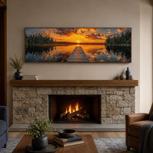 Puede incluir: Un cuadro panorámico de pared que muestra un muelle de madera extendiéndose hacia un lago tranquilo al atardecer, con nubes naranjas y amarillas reflejadas en el agua, enmarcado y montado sobre una chimenea de piedra con fuego encendido.