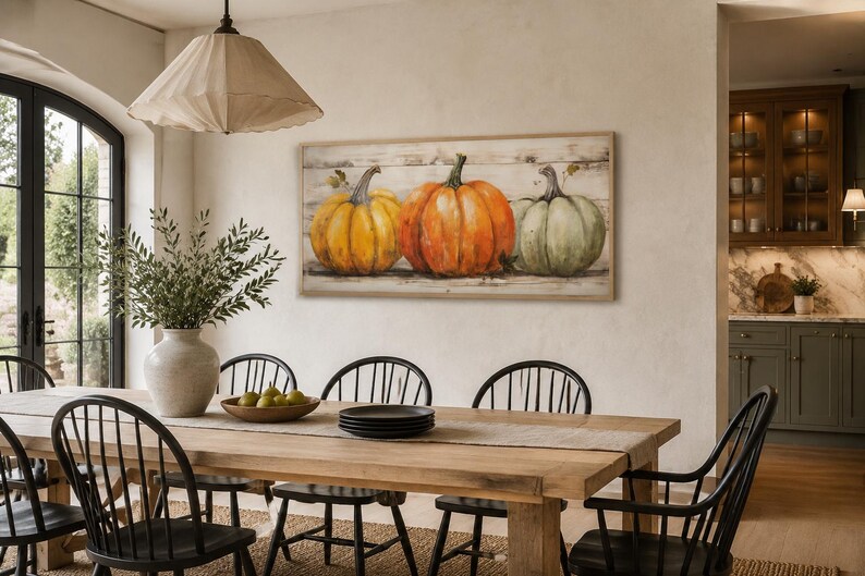 May include: A rectangular wall art piece featuring a painting of three pumpkins in yellow, orange, and muted green, set against a rustic white wood-plank background, enclosed in a light-toned wooden frame, displayed horizontally on a wall.