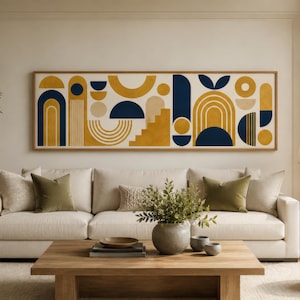 May include: A living room scene featuring a large abstract art piece with geometric shapes in mustard yellow and navy blue. A white sofa with olive green pillows sits below the artwork. A wooden coffee table and a potted olive tree complete the decor.