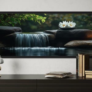 A framed photograph of a serene waterfall scene with white flowers on rocks is displayed on a wall above a wooden dresser with a lamp, books, and a clock.
