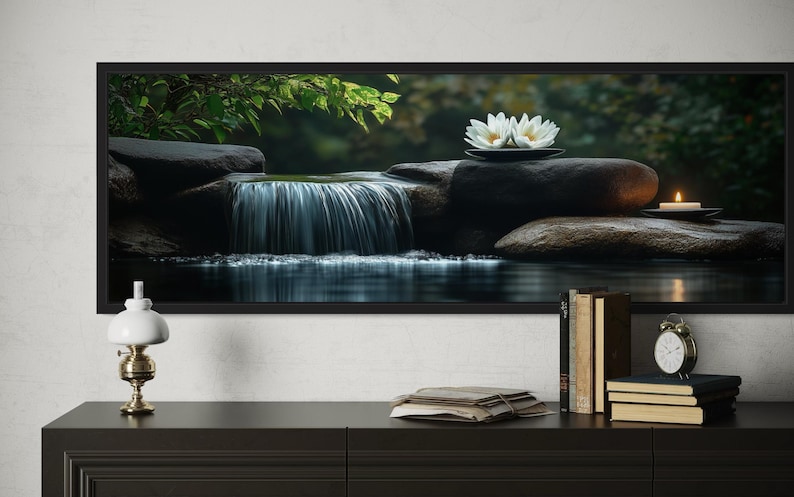 A framed photograph of a serene waterfall scene with white flowers on rocks is displayed on a wall above a wooden dresser with a lamp, books, and a clock.