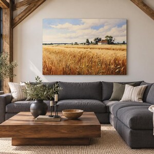 May include: A large rectangular landscape painting depicting a golden wheat field under a blue sky with white clouds, mounted on a white wall above a dark gray sectional sofa, a wooden coffee table, and a woven rug in a bright living room.