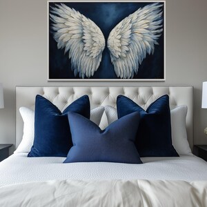a bedroom with a large bed, white bedding, and blue accent pillows. Above the bed is a framed artwork of white and blue angel wings. On either side of the bed are nightstands with black lamps, and there are white flowers on the nightstands.