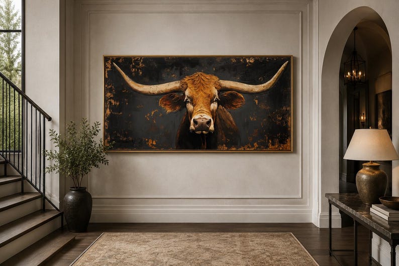 May include: A large rectangular wall art piece featuring a detailed portrait of a brown longhorn cow with prominent horns. The animal is set against a dark, textured background with hints of gold and bronze tones, framed in a thin gold frame.