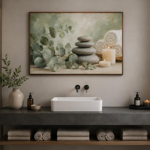 May include: A rectangular wall art print featuring a stack of smooth grey stones, green eucalyptus branches, white rolled towels, and two lit pillar candles. The artwork is displayed in a thin brown frame above a white rectangular bathroom sink.
