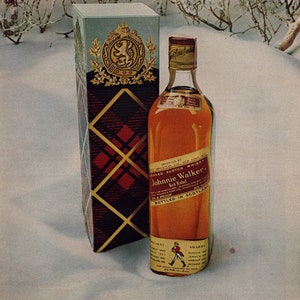 May include: A bottle of Johnnie Walker Red Label Scotch whisky with a red and gold label. The bottle is sitting on a snowy surface with a box behind it. The box is red and gold with a plaid pattern. The text on the bottle reads "Imported by Somerset Importers, Ltd., New York, N.Y.". The text on the box reads "Johnnie Walker Red Label Blended Scotch Whisky 86.8 Proof."