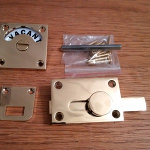 May include: Brass door hardware set featuring a 'VACANT' sign, a latch, and a strike plate. The set comes with screws for installation.