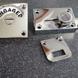 May include: Chrome door latch with a square plate that says "ENGAGED" on the front. The latch has a sliding mechanism and a round knob.