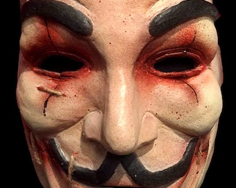 May include: A white mask with black painted features, including a moustache and goatee. The mask has red painted details around the eyes and mouth, resembling stitches and blood.
