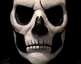 May include: A white skull mask with black eye sockets and a painted black mouth. The mask has a detailed, realistic design.