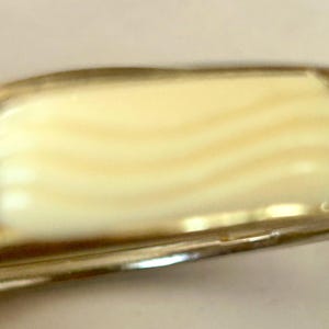 May include: Close-up of a pocket knife handle. The handle is a light cream color with a wavy pattern, framed by a silver-colored metal. The knife appears to be vintage or antique.