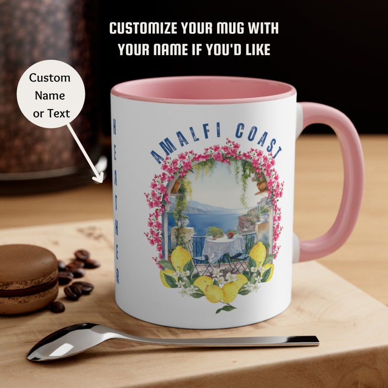 May include: White ceramic mug with a pink rim. The mug features a colorful illustration of a balcony overlooking the Amalfi Coast with lemon trees and the text "Amalfi Coast".
