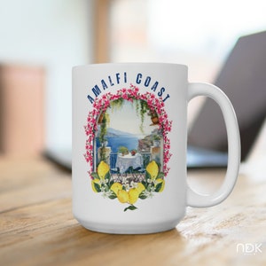 May include: White ceramic mug with a colorful illustration of a balcony overlooking the Amalfi Coast. The illustration features a table with chairs, lemons, and flowers. The text "Amalfi Coast" is printed in blue on the mug.