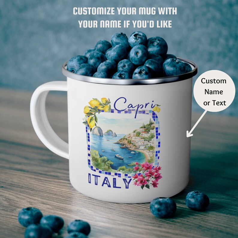 May include: White enamel mug with a colorful illustration of Capri, Italy. The mug has a blue handle and a silver rim. The illustration features a seaside town with buildings, boats, and a lemon tree. The text "Capri" and "ITALY" are printed on the mug.