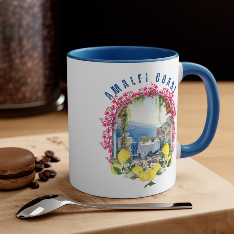 May include: White ceramic mug with a blue rim and handle. The mug features a colorful illustration of a lemon tree with lemons and flowers, a view of the ocean, and the text "Amalfi Coast".