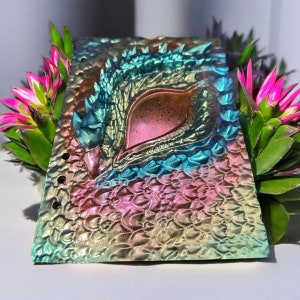 May include: A iridescent pink, green, and gold dragon eye notebook cover with a textured, scaly design.
