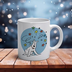 May include: A white ceramic mug featuring a graphic illustration of a white dog with a black nose and ears, surrounded by colorful stars and swirling lines against a circular blue background, with a handle on the right side of the mug.