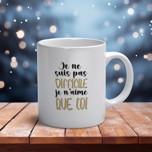Può includere: Tazza in ceramica bianca con un design nero e oro. Il testo sulla tazza recita "Je ne suis pas difficile je n'aime que toi".