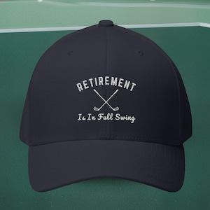 May include: A navy blue baseball cap featuring the white text "RETIREMENT Is In Full Swing" and crossed golf clubs. This cap is a classic design, suitable for golf lovers or as a retirement gift.