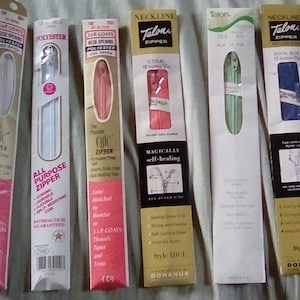 May include: Six packages of different zipper brands and styles. The packages are white with colourful zipper samples inside. The packages have text that says "Talon Zipper", "Chic Zipper", "All Purpose Zipper", "Magically Self-Healing", "Neckline Zipper", and "Style 110-1 Donahure".