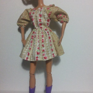 May include: A doll wearing a beige dress with a floral pattern and purple boots.