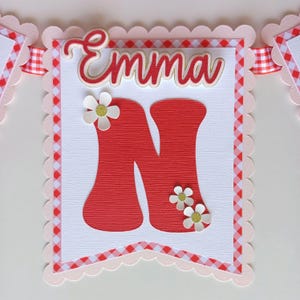 May include: A pink and red gingham banner with white scalloped edges. The banner has the name "Emma" and the letter "N" in red with white daisies.