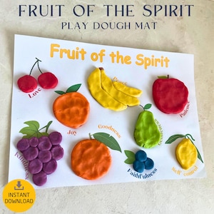 May include: A white play dough mat with the text "Fruit of the Spirit" and colorful play dough fruits. Includes cherries, bananas, an orange, an apple, a pear, grapes, blueberries, and a lemon. The words "Love", "Joy", "Kindness", "Goodness", "Faithfulness", "Gentleness", "Self control", "Patience", and "Peace" are written on the mat.