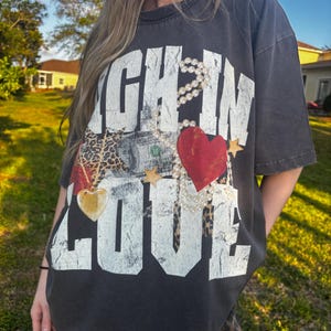 May include: A black t-shirt with a white graphic that says "Rich in Love" with a red heart, a gold heart, a money bill, and a leopard print pattern.
