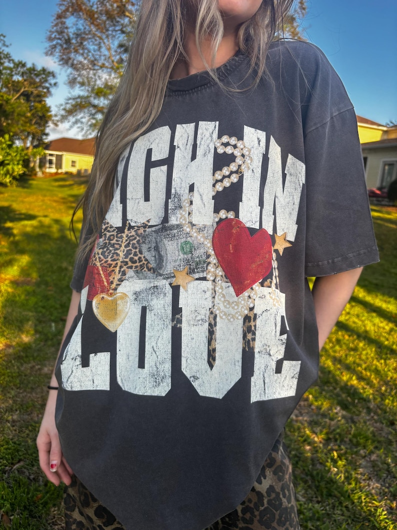 May include: A black t-shirt with a white graphic that says "Rich in Love" with a red heart, a gold heart, a money bill, and a leopard print pattern.