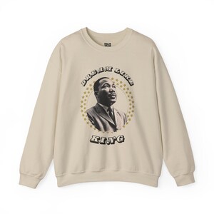 May include: Cream-colored sweatshirt featuring a portrait of Martin Luther King Jr. within a star-studded circle. The words "DREAM LIKE KING" are arched above and below the portrait in a vintage font. The sweatshirt has long sleeves and a crew neck.