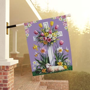 Könnte beinhalten: Eine violette Osterflagge mit einem weißen Kreuz, das mit rosa, gelben und weißen Blumen geschmückt ist. Ein weißes Lamm liegt am Fuß des Kreuzes.