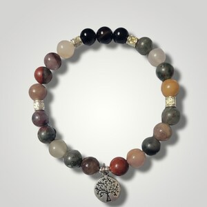 Puede incluir: Una pulsera de cuentas con una variedad de piedras preciosas de colores, incluyendo cuentas rojas, marrones, verdes y negras. La pulsera tiene espaciadores plateados y un dije plateado con un diseño de árbol. La pulsera está diseñada para usarse alrededor de la muñeca.