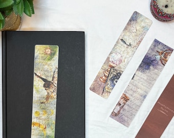 May include: Set of four bookmarks featuring watercolor illustrations. One bookmark features a bird in flight, another features a compass, another features an hourglass, and the last features a book and a crystal ball. The bookmarks are all rectangular and have a white background.
