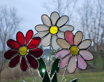 May include: A stained glass bouquet of three flowers with red, white, and pink petals. The flowers have yellow centers and green leaves.