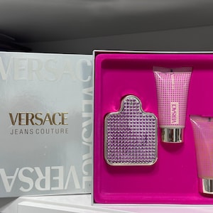 Op de afbeelding: Een roze cadeauset met een zilveren en paarse fles Versace Jeans Couture parfum, een roze lotionfles en een roze douchegel fles.