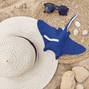 Puede incluir: Un sombrero de paja blanco con un diseño de raya manta azul y blanca con lunares. El sombrero está sobre una estera de paja tejida con gafas de sol y conchas.