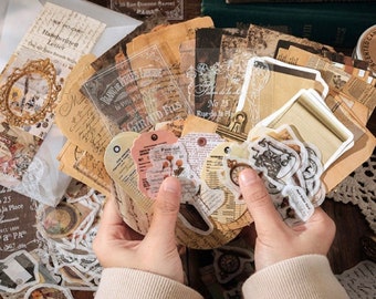 May include: A collection of vintage-themed paper ephemera, including tags, stickers, and decorative paper packets. The packets feature various designs, including a starry night scene and handwritten letters. The items are arranged on a wooden surface.