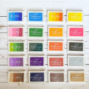 Könnte beinhalten: Ein Set mit 16 Stempelkissen in verschiedenen Farben, darunter Blau, Grün, Rosa, Orange, Gelb, Lila und Braun. Die Stempelkissen sind mit "Let's Color" und "Craft Ink Pad" beschriftet.