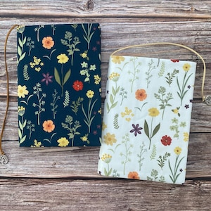 May include: Two book covers with floral patterns. One cover is dark blue with yellow, orange, and red flowers. The other cover is white with yellow, orange, and red flowers.