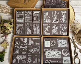 May include: A set of nine brown wooden rubber stamps with white ink designs. The stamps feature floral designs, a guest check, and postage stamps. The stamps are arranged in three rows of three in a wooden box.