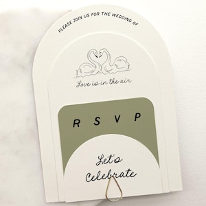 May include: A white RSVP card with a green RSVP section and a white section with the text "Let's Celebrate". The top section of the card features a pair of swans with the text "Please join us for the wedding of Love is in the air".