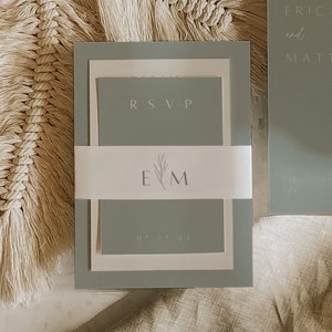 May include: A sage green wedding invitation suite with a white RSVP card and a white card with the initials "E & M" and a small floral design. The date "07.17.23" is printed on the bottom of the card.