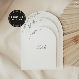 May include: White arch-shaped cards with the text "together with their families", "Details", "RSVP", and "L&K" in black calligraphy. The cards are stacked on top of each other and are on a beige background. The text "PRINTING AVAILABLE" is in a black circle.