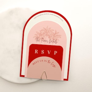 Può includere: Biglietto d'invito a strati con schema di colori rosso, rosa e bianco. La carta presenta il testo "OUR FAVORITE PEOPLE | OUR FAVORITE PLACE", "The Finer Details", "RSVP" e "MEET US IN the Keys". Una clip in metallo argentato tiene la carta.